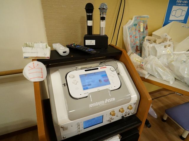 カラオケ機器のある部屋 共有スペース 歌を楽しむ設備が整った多目的室です。マイクやリモコンが置かれ、レクリエーションの一環としてご活用いただけます。