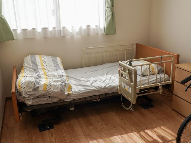 居室の一角とベッド 介護ベッド 明るく落ち着いた雰囲気の個室です。高さ調節が可能な介護ベッドが備え付けられ、快適な生活空間が確保されています。