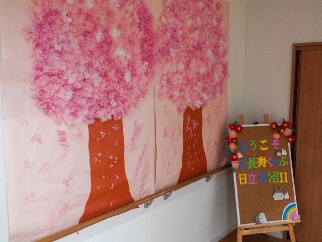 桜の木と掲示板の飾り 創作物 壁には桜の木の装飾があり、季節の移ろいを感じさせます。そばの掲示板はカラフルで心が和む工夫がされています。