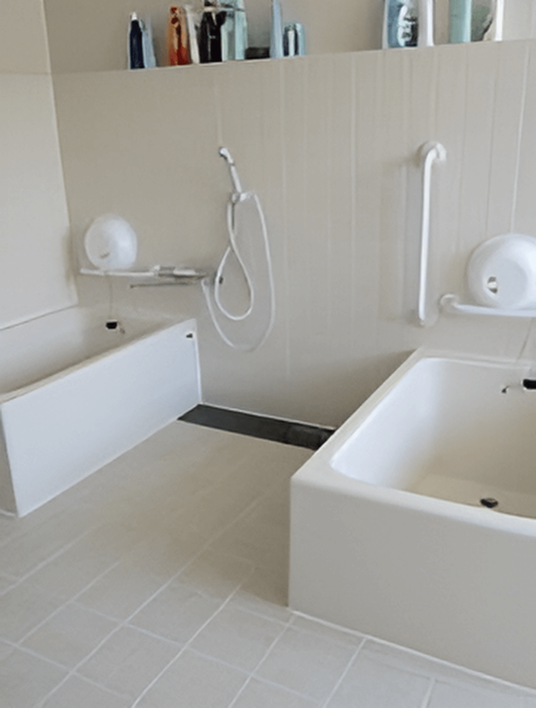 白い一人用の浴槽が二つ置かれた洗い場の広い浴室。それぞれの浴槽のそばには手すりが付いている。
