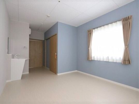 ライトブルーと白の壁がさわやかな雰囲気の居室。洗面所やトイレが付き、居室のドアは引き戸。