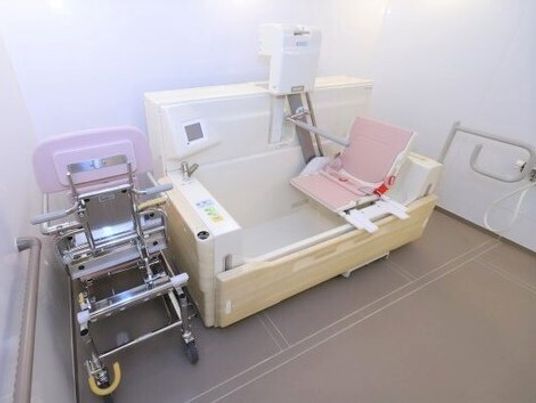 白とピンクの機械浴が置かれたタイル張りの浴室。重度の人も入浴できる設備があり、壁には手すりが付いている。