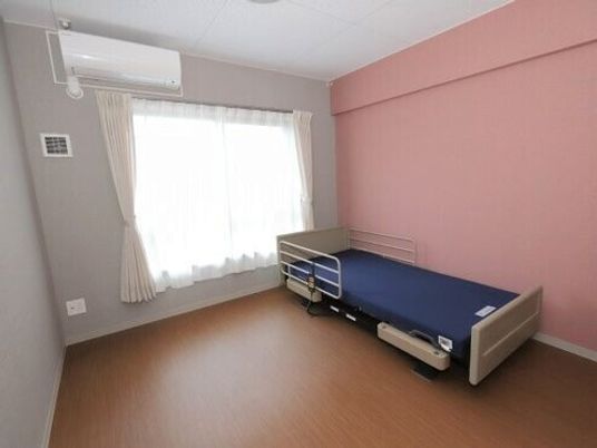 フローリングのシンプルな居室。エアコンやカーテン付きの窓、寝具付きのベッドなどが付いている。