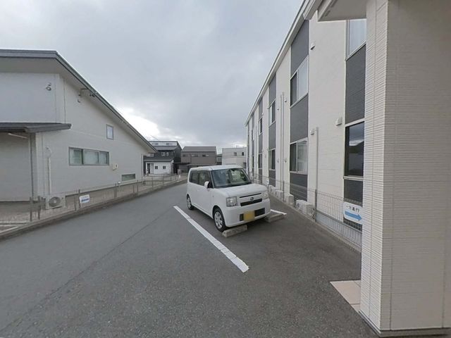 白い壁の建物と駐車場 外観 広々とした駐車スペースがある清潔感のある建物です。快適なアクセスをお約束します。