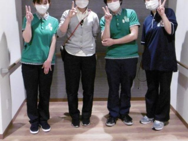 スタッフが並ぶ廊下 廊下   廊下でスタッフの方々が並び、笑顔で手を上げています。明るい通路で、連携のよさが伝わります。