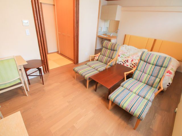 居室の明るい空間 居室 広々とした居室は、優しい色合いで落ち着いた雰囲気を醸し出しており、ゆったりとした時間を過ごすことができます。木目調の床や家具があたたかい印象を与え、快適な生活空間を提供しています。