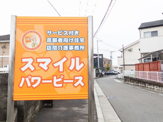 看板の前の通り風景 看板 明るい色合いの看板が、温かな雰囲気をお知らせしています。この地域での新たなキャリアを考える一歩として、ぜひご覧ください。