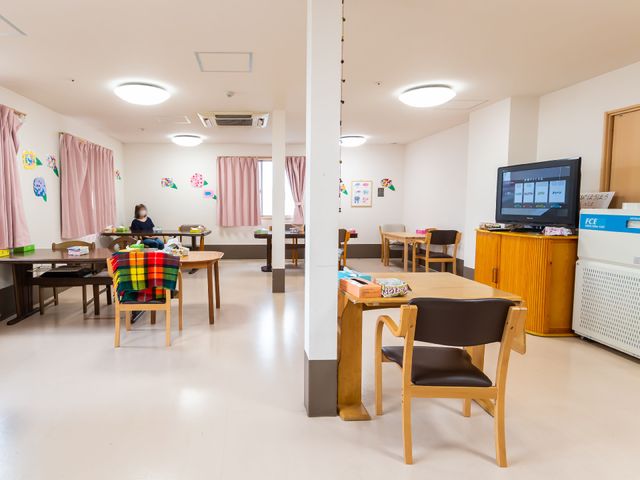 共有スペースの日常風景 食堂 ゆったりとした多目的室で、一人が読書に集中しています。周りには、カラフルなクッションやテレビなどの娯楽が少なからずあります。