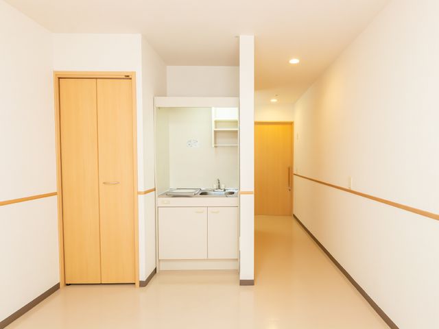 廊下と小さなキッチン 居室 綺麗に保たれた廊下には、足元に安全を考慮した手すりが設置されており、温かみのある照明が心地よい雰囲気を醸し出しています。手元には簡易的なキッチンもあり、快適な生活空間づくりに配慮されています。