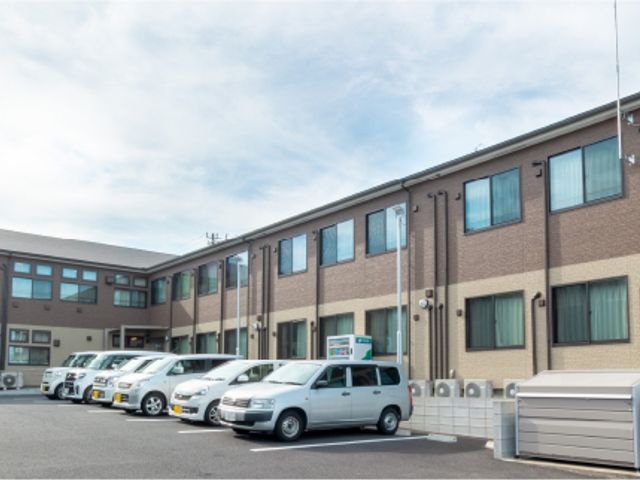 車が並ぶ施設の建物 外観 明るい空と広々とした駐車スペースが特徴の建物です。車でのアクセスが便利です。