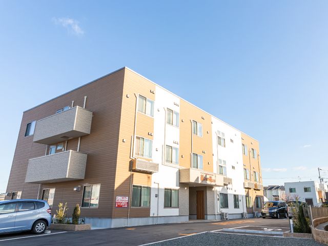 新築そうな外観 外観 平坦な駐車場を備えた清潔感のある建物です。外壁の色合いやデザインが、快適な環境を提供していることを物語っています。