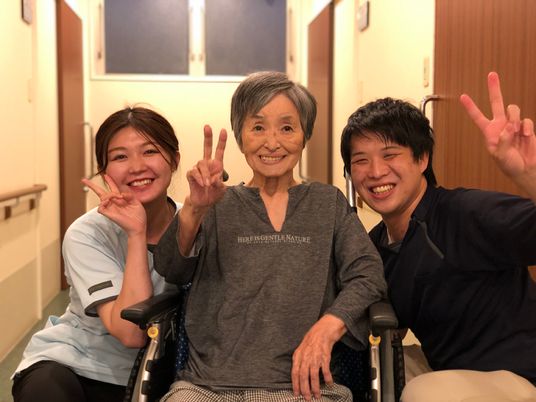 車椅子に座った女性利用者の両脇にスタッフが座っている、３人でピースをしている様子