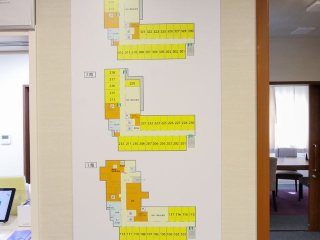 配置図が掲示された廊下 館内案内 丁寧に掲示された配置図が、利用者様の移動をサポートします。見やすく整理された情報は、働くスタッフにも役立ちます。