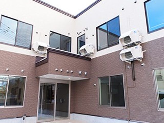 明るい中庭の外観 中庭   中庭に面した2階建ての建物で、窓が多く明るい印象です。出入りしやすい通路まわりも見え、働く場の雰囲気が伝わります。