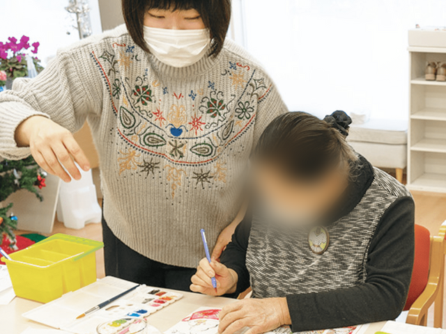 塗り絵を楽しむ女性とスタッフ 多目的室 スタッフが一緒に塗り絵を楽しむ様子です。アクティビティを通じて居住者の表現活動を支援します。