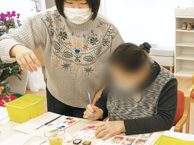 共に絵を描く様子の室内 多目的室 広々としたスペースで、スタッフと共に創作活動を楽しんでいます。自然光が心地よく差し込む空間です。