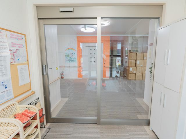 居室の入り口 居室 広々とした入り口の前に、リラックスできる椅子がございます。入居者に配慮した温かい空間です。