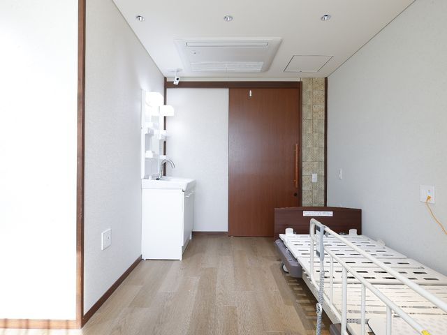 シンプルな洗面台とベッド 居室 ゆったりとした居室で、洗面台も完備されています。清潔感のあるこの空間で快適な毎日をお過ごしいただけます。