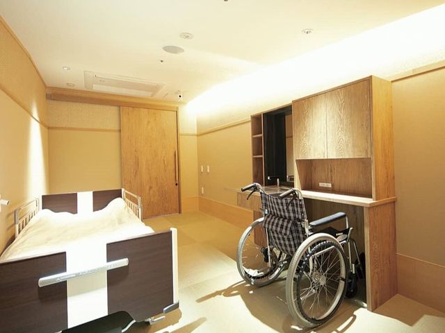 広々とした居室と車椅子 居室 広々とした居室には必要な家具が整っており、日当たりの良い窓も配されています。機能的な広さは、快適な個人スペースを確保しています。