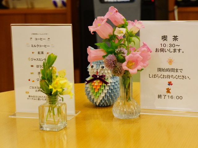 フロントの花と掲示物 喫茶スペース・メニュー 温かみのあるフロントには、きれいな花が飾られ、優しい気配りを感じる案内があります。ゆったりとした時間が流れる空間です。