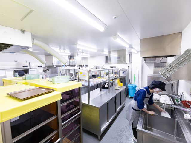 清潔なキッチンの様子 キッチン 効率の良い動線を確保したキッチンで、スタッフが清掃を行っている様子が見受けられます。食事の準備や清掃における日々の業務をイメージしていただけます。