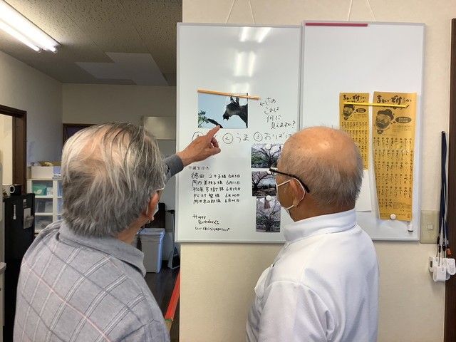 掲示がある廊下 掲示物 掲示物を前に話し合う場面です。情報共有を通じて、働きやすい環境が整っています。