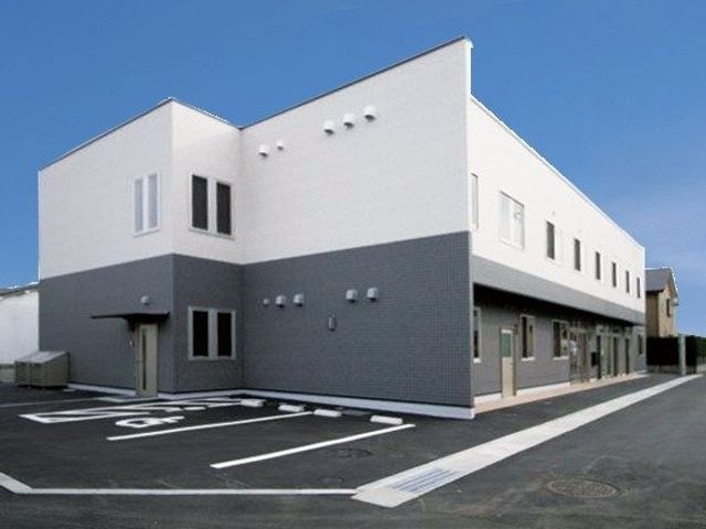建物外観 外観   白とグレーの落ち着いた外観で、駐車スペースも見えます。就業時の出入りがしやすそうな建物です。