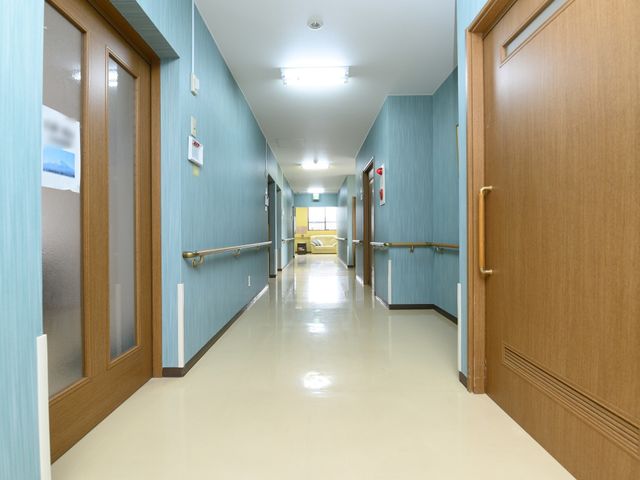 清潔感のある廊下 通路 手すり完備で安全な通路です。奥に見える共有スペースでは、職員と利用者さまの穏やかな交流が見受けられます。