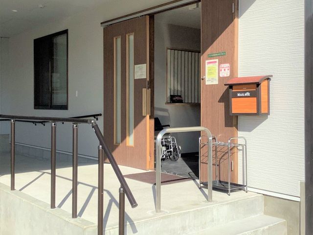 エントランスと手すり 玄関 日差しが差し込む温もりのあるエントランスです。車椅子用のスロープも完備され、アクセスに配慮が見られます。