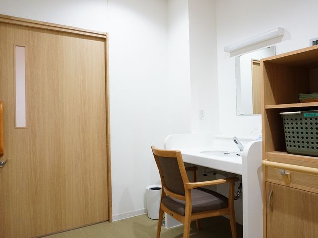 居室の洗面台とドア 洗面台 ゆとりのある清潔な洗面台が完備された個室で、快適な生活環境が整っています。手すりも設置され、安全に配慮された空間です。