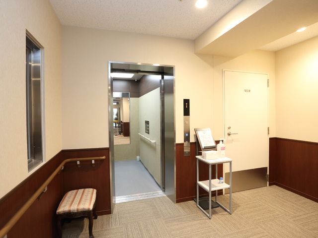 清潔な施設のエレベーター エレベーターホール 手すり付きの廊下はバリアフリー設計で、スタッフも利用者様も快適に移動できます。明るく清潔な空間が皆様をお迎えいたします。