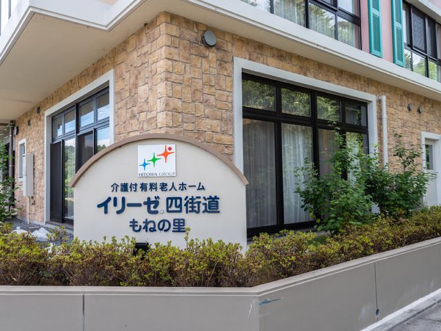 石造りの外観 ロゴ 落ち着いた色合いの建物正面には、植栽が配され、温かみのある雰囲気を醸し出しています。