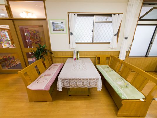 木製のテーブルとベンチにはそれぞれ、敷布が掛けられている。テーブルの上には本が置いてある。観葉植物が飾られている。