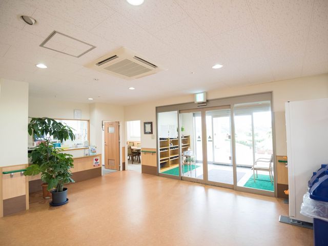 広々とした明るいエントランス 玄関 居心地の良い開放的なエントランスです。待合いには緑の植物が飾られ、来訪者を温かく迎えています。