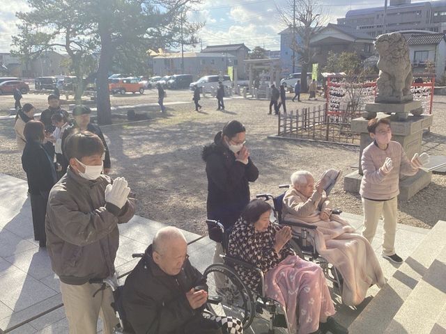 祈る入居者とスタッフ 庭 広々とした庭で、入居者とスタッフが一緒に手を合わせて穏やかな時間を過ごしています。