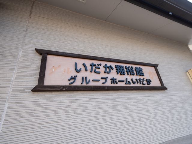 施設の外壁に取り付けられた看板 看板 温もりを感じる木の看板が目を引きます。こちらで働くと、訪れる方々の安心感に繋がるでしょう。
