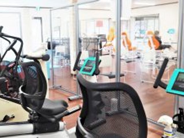 トレーニング器具と机のある部屋 機能訓練室 自然光が差し込む訓練室では、リハビリ用の機器と机が配置されており、効率的なトレーニング環境が整っています。