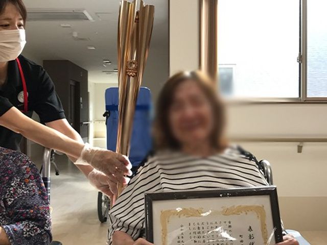 認定証を受け取る様子の部屋 内観 明るい空間で、スタッフが利用者に賞状を手渡しています。自然光が差し込む穏やかな場所です。