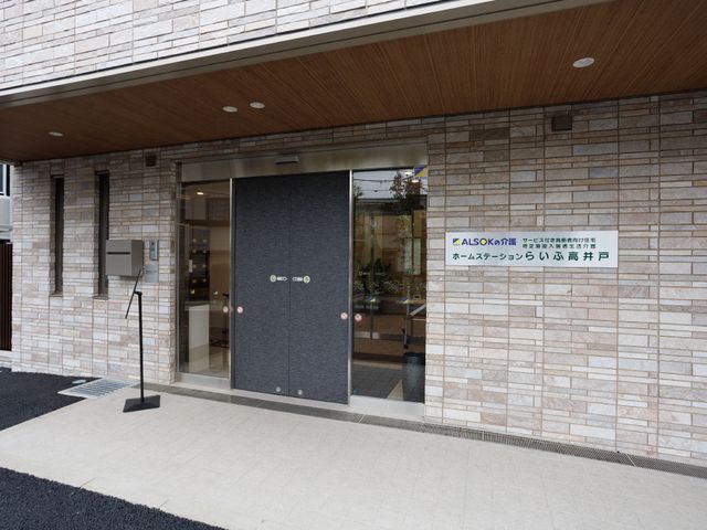 綺麗な施設のエントランス 玄関 落ち着いた色合いのエントランスは、訪れる方を優しく迎え入れます。手前には案内板も設置され、訪問者の目印となっています。