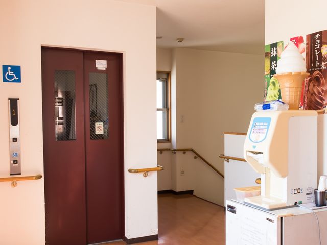 エレベーター付近の廊下 エレベーター 手すり付きの廊下にはソフトクリーム機が設置され、ひとときの憩いの場を提供しています。バリアフリーの配慮が見受けられるエレベーター付近です。