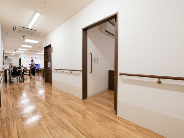 施設の明るい廊下 廊下 手すりが取り付けられた廊下を通り、ゆったりとしたスペースで寛がれる方がいらっしゃいます。天井の照明が良く、清潔感のある環境を提供しています。
