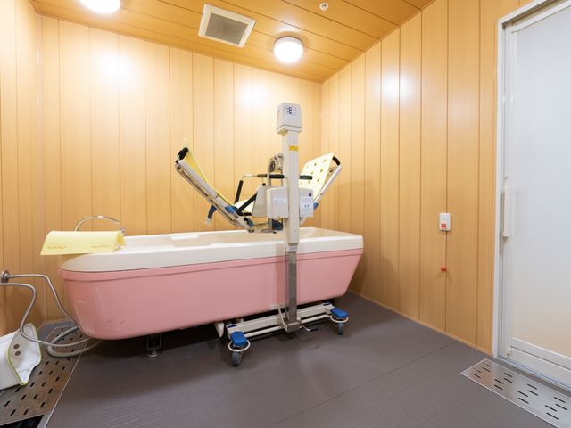 特殊浴槽の設備 特殊浴槽室 清潔感のある木目調の壁に囲まれた浴室に、安全かつ快適な入浴を支援する特殊浴槽が設置されています。サポートが必要な方も安心してご利用いただける環境が整っております。