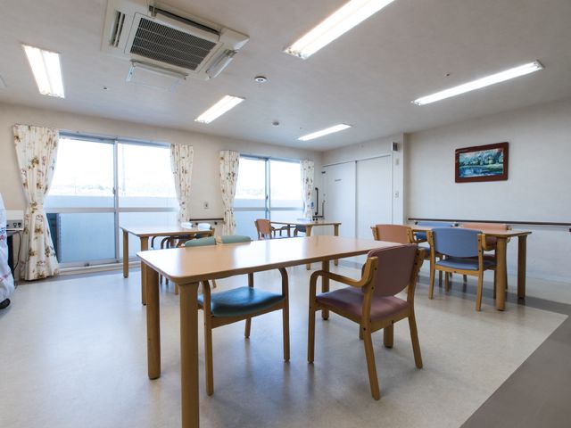 明るいダイニングスペース 食堂2 日差しの入るダイニングで、ご入居者様が食事やコミュニケーションを楽しまれています。窓際には彩り豊かなカーテンが、温かみのある空間を演出しております。