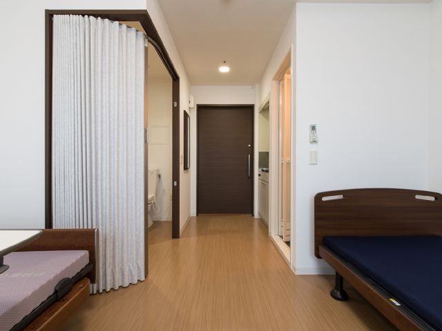 居室のベッドとドア 居室 ゆったりとしたベッドと広々とした出入り口が特徴の居室です。清潔感のある明るい空間で、日々の生活が快適に過ごせそうです。
