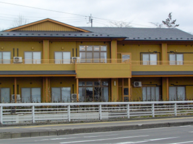 建物外観 外観   落ち着いた色合いの2階建てで、前面には広い道路と白い柵が見えます。就業先の雰囲気を外から確認しやすい佇まいです。