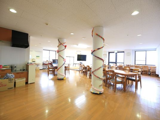 施設の写真 中央に大きな白い柱が２本立ったダイニングである。柱にはらせん状に飾りつけがされている。奥にテーブルセットが並んでいる。
