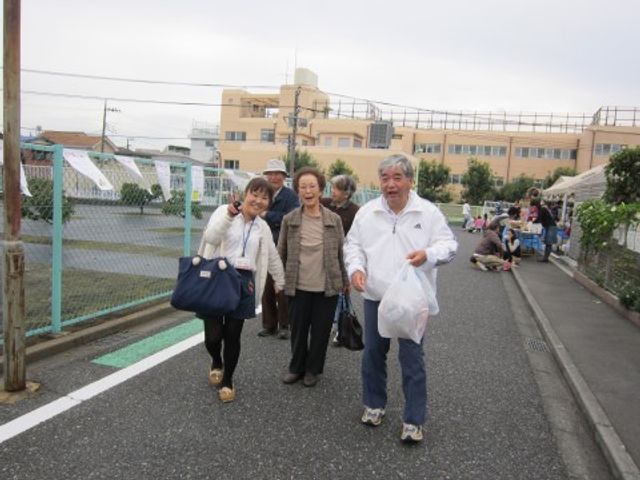 散歩する楽しげな高齢者たち 周辺環境 笑顔で手を振る高齢者たちが、広々とした外の空間を歩いて楽しんでいます。あたたかな共同のひとときを共有しています。