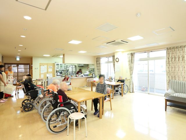 快適な食堂の様子 多目的ルーム 明るく広々とした空間で利用者が食事や談話を楽しんでいます。スタッフの方が笑顔で対応している姿も見受けられます。