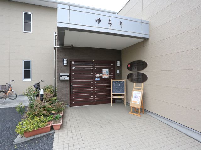 エントランスの外観写真 施設入口 植栽に囲まれた清潔感のある入口です。外には掲示板が設置され、日々の情報共有に活用されています。