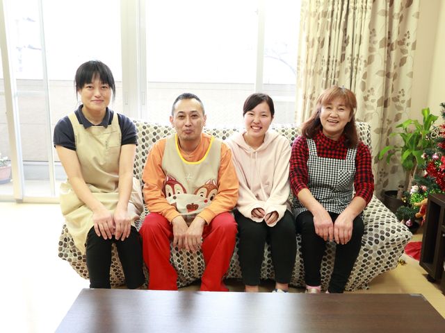 明るいリビングの集合写真 スタッフ 笑顔で対面するスタッフたち。温かみのある空間でのふれあいが、仕事のやりがいを感じさせます。